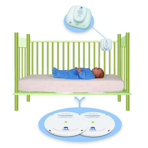 Baby lying in a green crib with monitoring devices above and below, illustrating a baby monitoring system.
