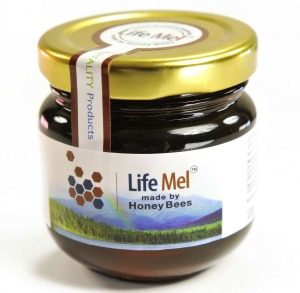 A jar of Life Mel honey with a gold lid. The label features a honeycomb design, the words “Life Mel made by Honey Bees,” and an image of a green landscape with mountains in the background.