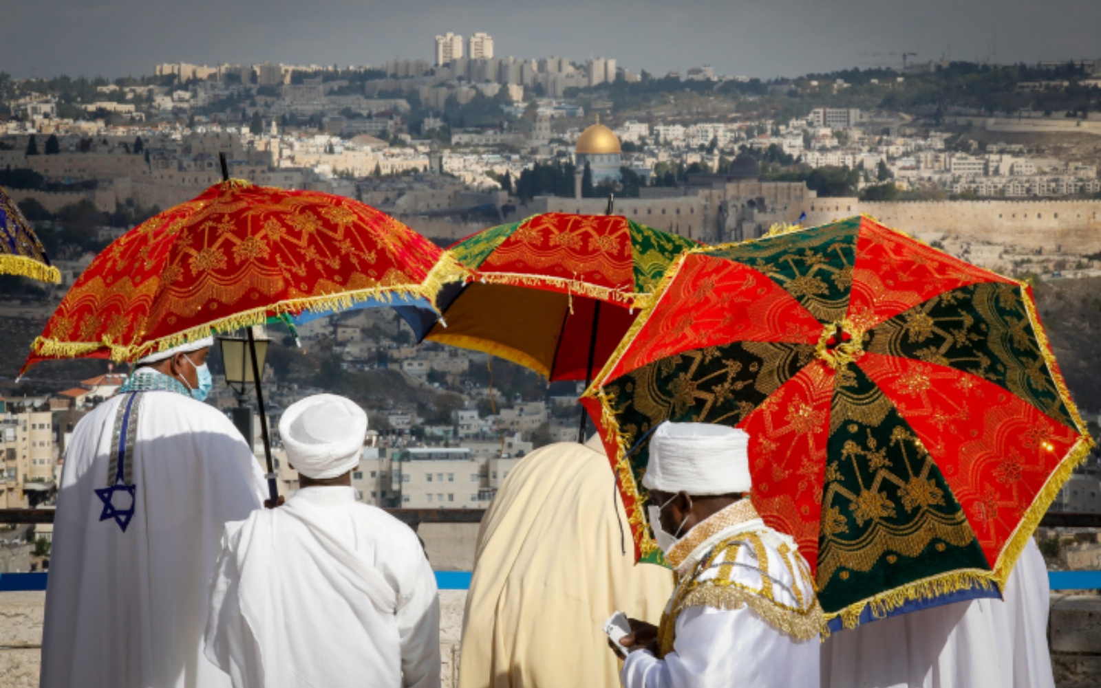 People take in the view from the promenade at the Ethiopian Jewish community’s annual Sigd celebration in Jerusalem. Photo by Olivier Fitoussi/Flash90 People dressed in white robes, some adorned with an Israeli flag, stand under ornate red and gold umbrellas, overlooking the cityscape of Jerusalem's Old City, the background includes the Dome of the Rock in Jerusalem.