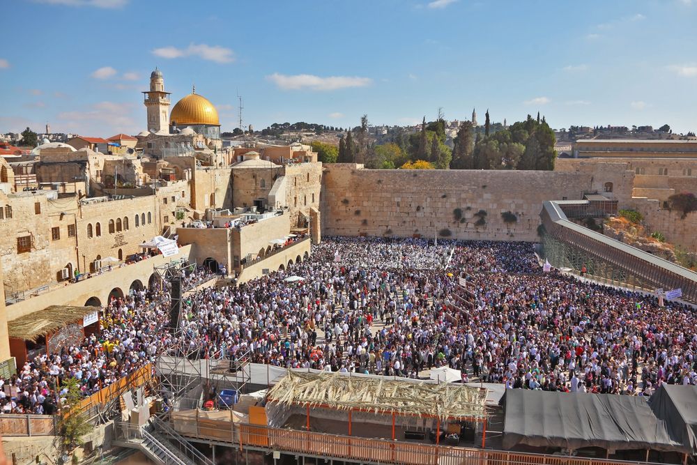 Tens of thousands of Jews gather for a pre-Yom Kippur mass prayer for forgiveness (slichot) at the Western Wall in Jerusalem's Old City. Photo via Kavram/Shutterstock.com A large crowd gathers at the Western Wall in Jerusalem, with the golden Dome of the Rock visible in the background under a blue sky with scattered clouds.
