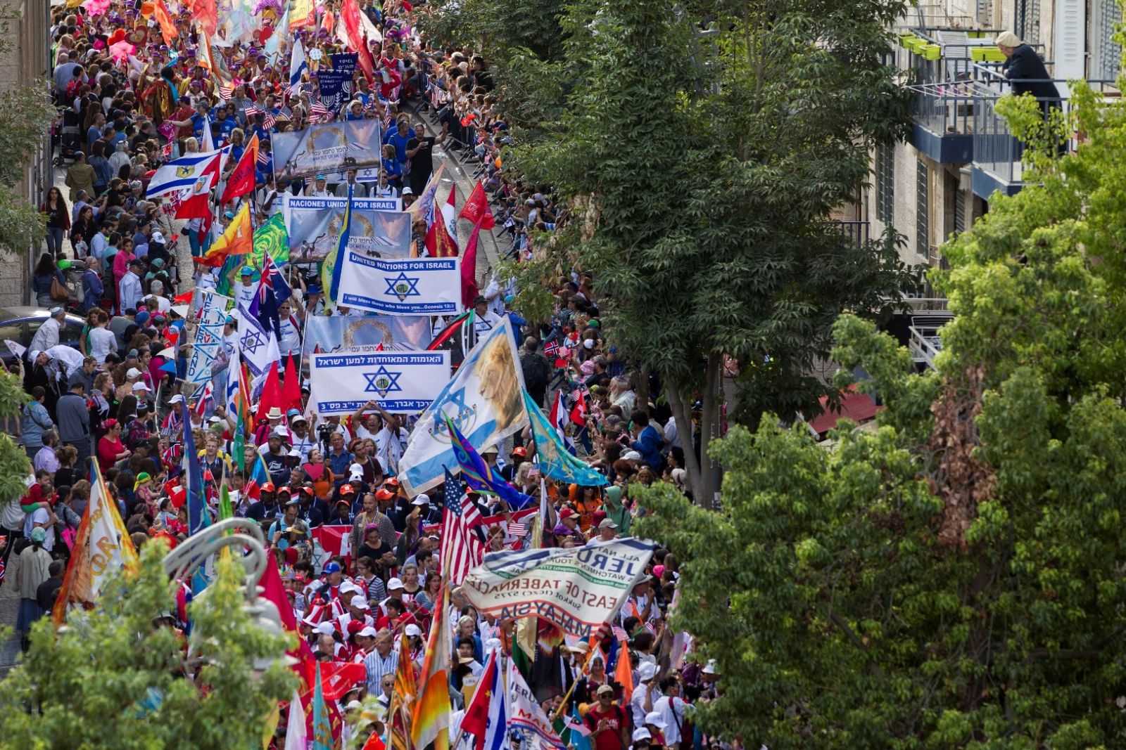 Tens of thousands of marchers parading through Jerusalem last Sukkot. Photo by Miriam Alster/FLASH90 A large crowd marches down a city street in Jerusalem carrying flags, banners with Israeli symbols, and colorful signs; trees line the street and people fill the scene, creating a festive atmosphere.