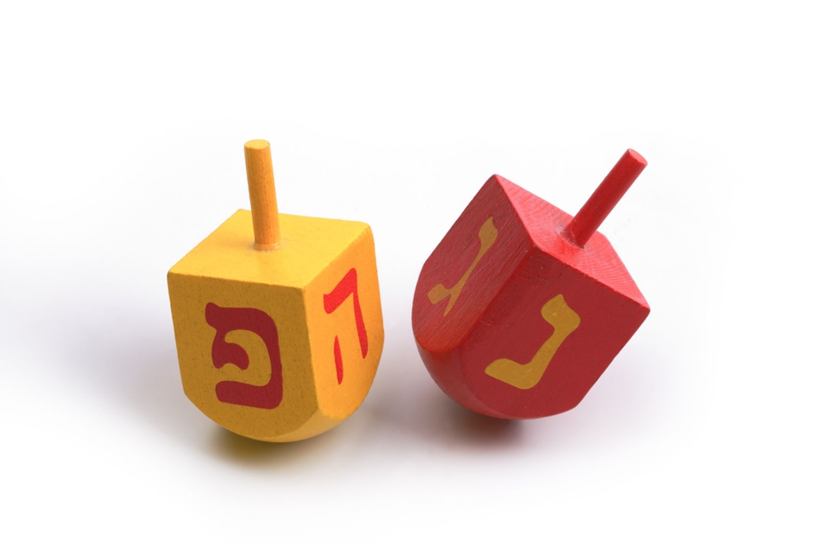 Two colorful dreidels, one yellow and one red, each with a Hebrew letter painted on one side, are standing upright on a white surface.