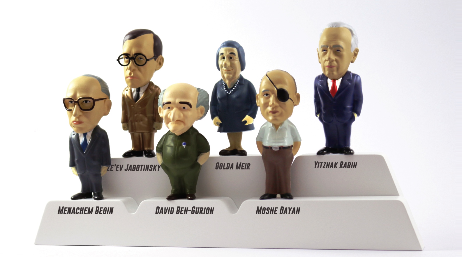 Piece of History Contemporary Jewish Gifts trivets. Photo: courtesy Six figurines of Israeli leaders stand on a white tiered display labeled with their names: Menachem Begin, Ze’ev Jabotinsky, David Ben-Gurion, Golda Meir, Moshe Dayan, and Yitzhak Rabin.