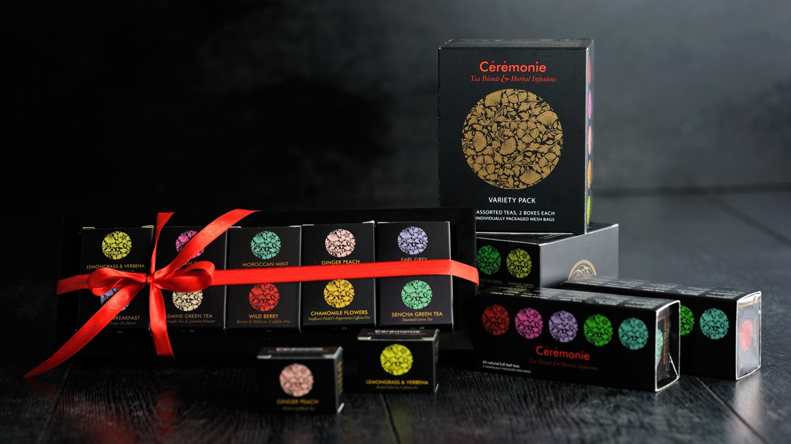Cérémonie Tea is set apart by attention to detail. Photo: courtesy Gift boxes of Cérémonie Tea in various sizes are arranged on a dark surface. One box is tied with a red ribbon, and the packaging features colorful circular patterns and gold detailing.