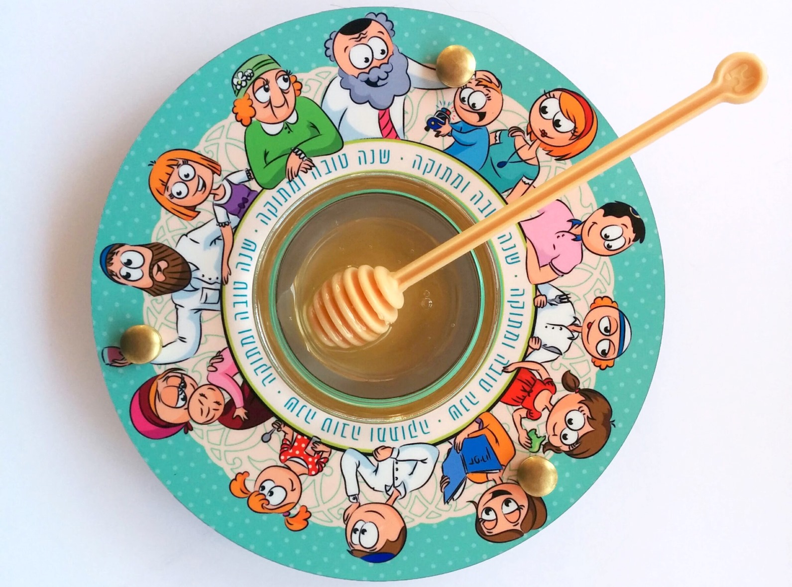 A bowl of honey with a honey dipper sits on a colorful plate featuring cartoon people and Hebrew text around the rim. The background is white.