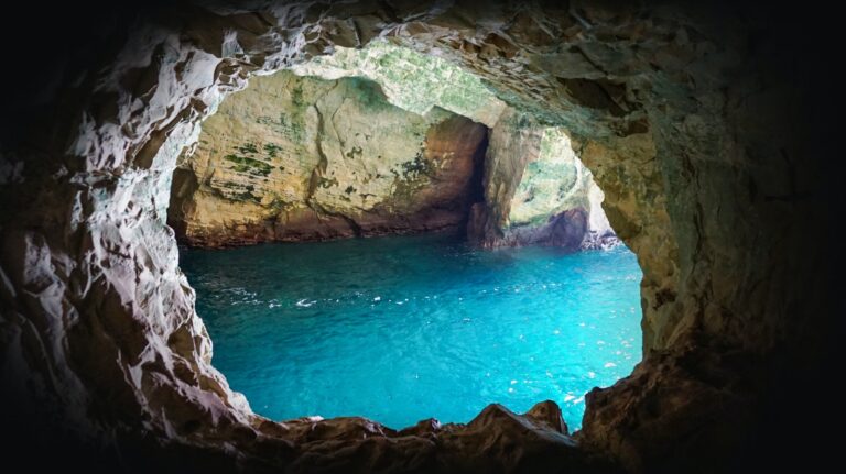 A view of the Grottoes in Rosh HaNikra, with bright blue water with sun shining on it. The water is framed by the the surrounding cave.