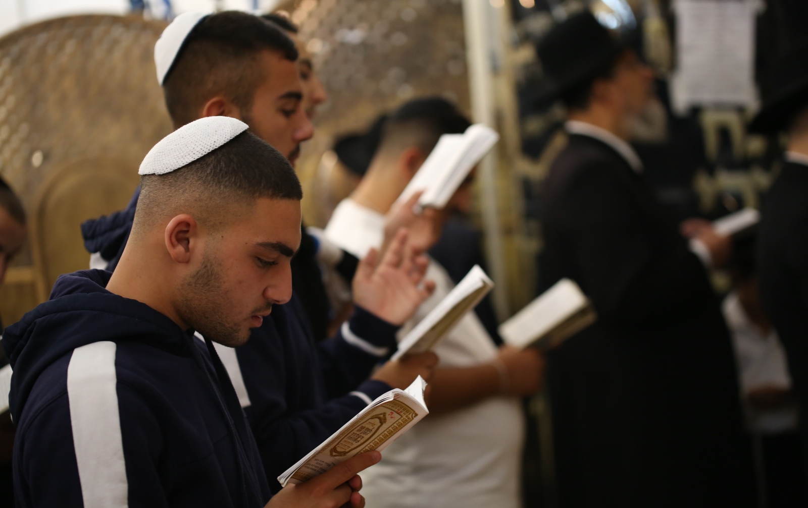 Some Israelis observe the High Holidays according to Jewish law, while others follow their own traditions. Photo by David Cohen/Flash90 Several young men wearing kippahs read from prayer books, standing closely together in a place of worship. The background shows other people, some in traditional Jewish attire, also engaged in prayer.