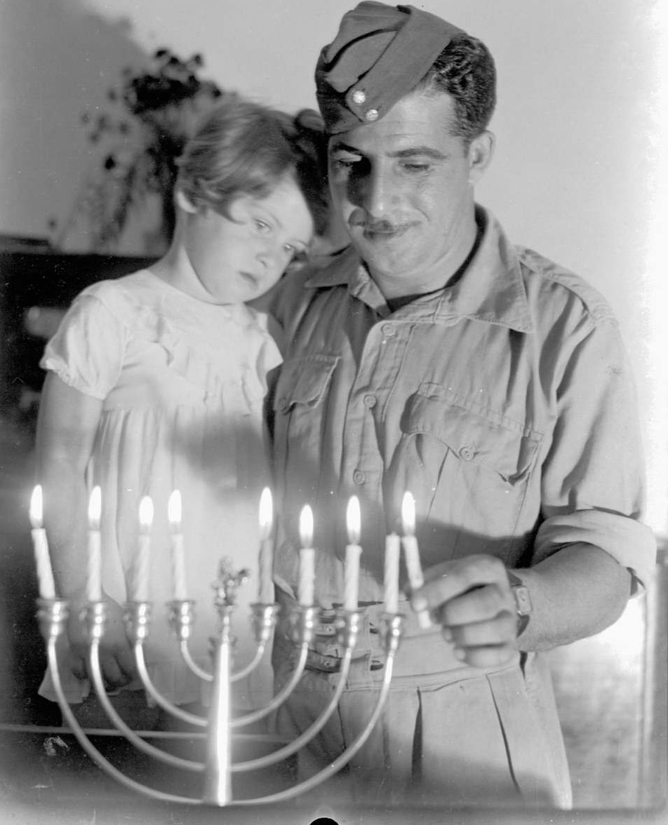 A soldier on leave while service in the British Army’s Jewish Infantry Brigade lights candles with his young daughter in 1941. Photo: GPO