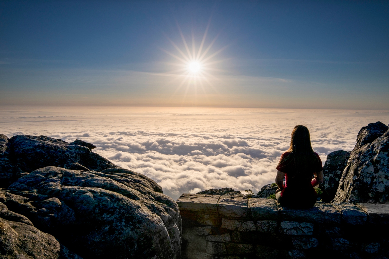 A woman watches as the sun sets above the clouds at the top of Tabletop Mountain in Cape Town, South Africa. Photo by Ilan Rogers