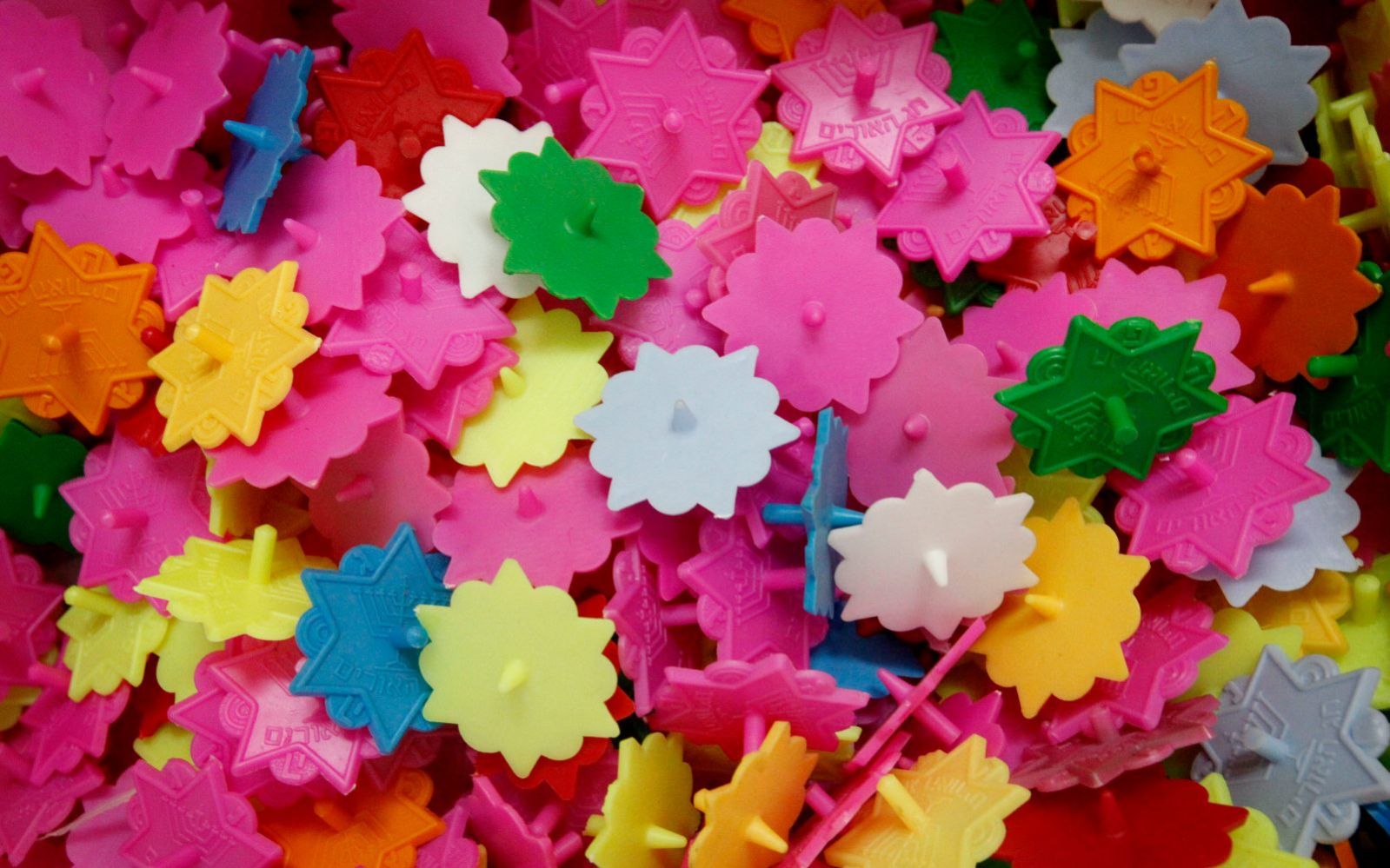 A pile of colorful, interlocking plastic dreidels, in shades of pink, white, yellow, green, orange, red, and purple.