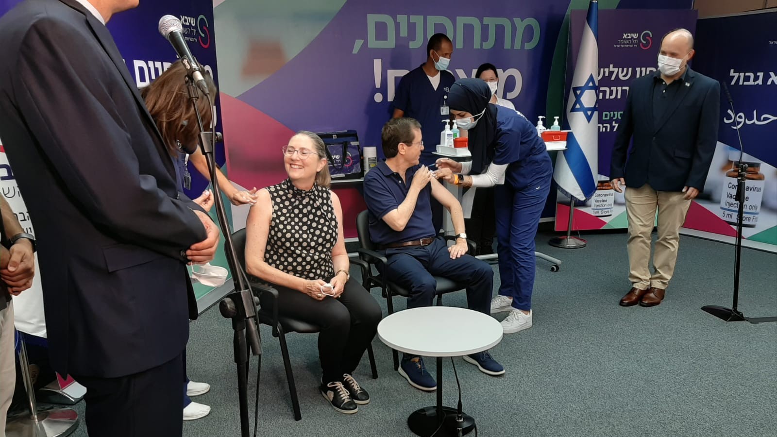 Sheba Medical Center nurse Lina Ahmad vaccinates President Isaac Herzog, 60, while his wife Michal waits her turn and Prime Minister Naftali Bennett (right) looks on. The Herzogs were first in the world to receive the third Pfizer vaccine as a booster, on July 30. Photo courtesy of Sheba Medical Center
