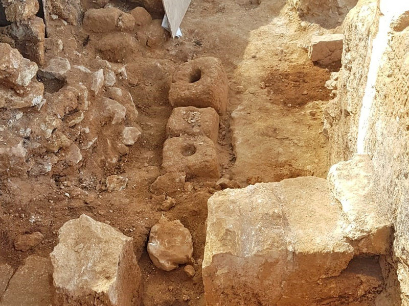 An ancient olive press uncovered at a 2,000-year-old Hasmonean village in Jerusalem. Photo © Ya`akov Billig/Israel Antiquities Authority An archaeological excavation site with three ancient stone toilet seats aligned in a row, surrounded by dirt and stone walls.