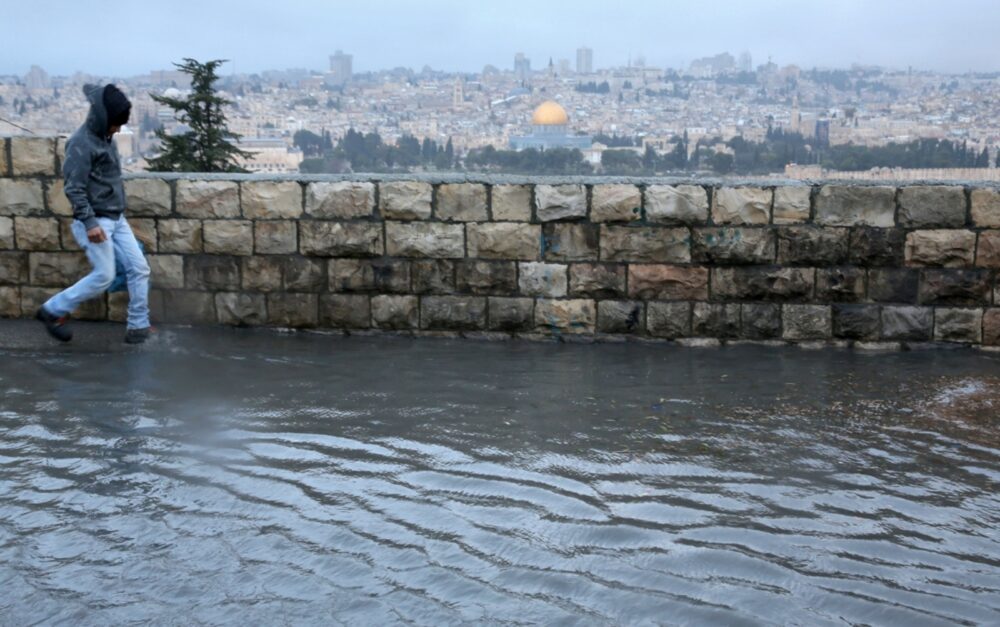 The Dome of the Rock is seen in the background of a young man in a flooded street after heavy rain hit Jerusalem. Photo by Nati Shohat/FLASH90