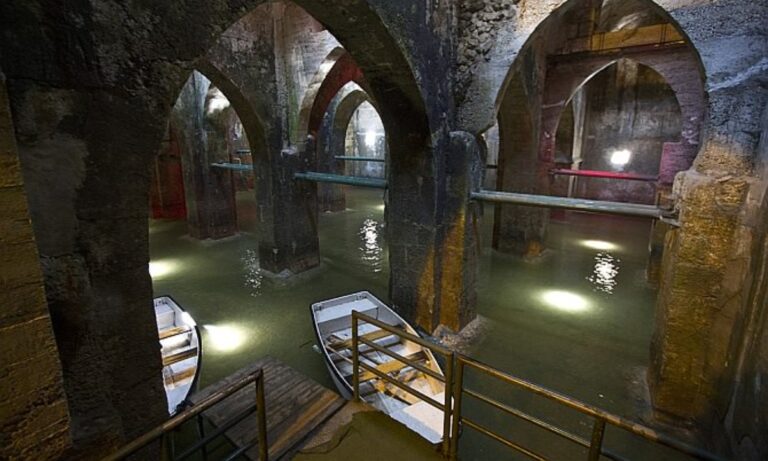 An image of Pool Arches in Ramla, featuring two empty row boats floating in the underground pools.. The boats sit peacefully among stone arches.