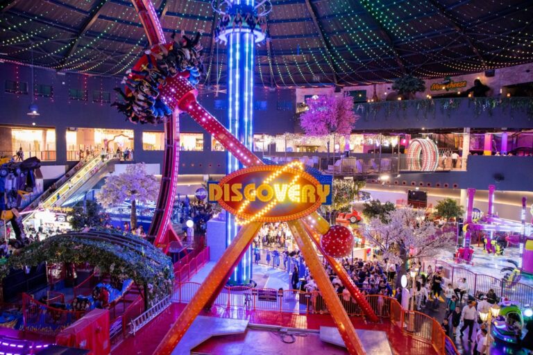 View of the interior of Magic Kass indoor amusement park showing hundreds of people walking around and a ride named "The Discovery" in action.