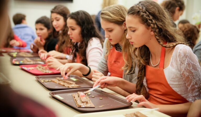 For young pre teen girls at a table wearing orange aprons and making chocolate.