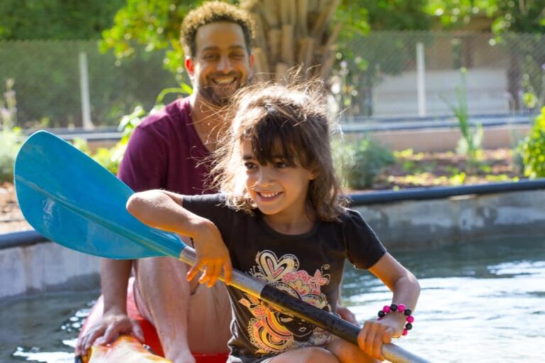 A young girl with brown hair smiling and kayaking with her father in the Shvil Hatapuzim