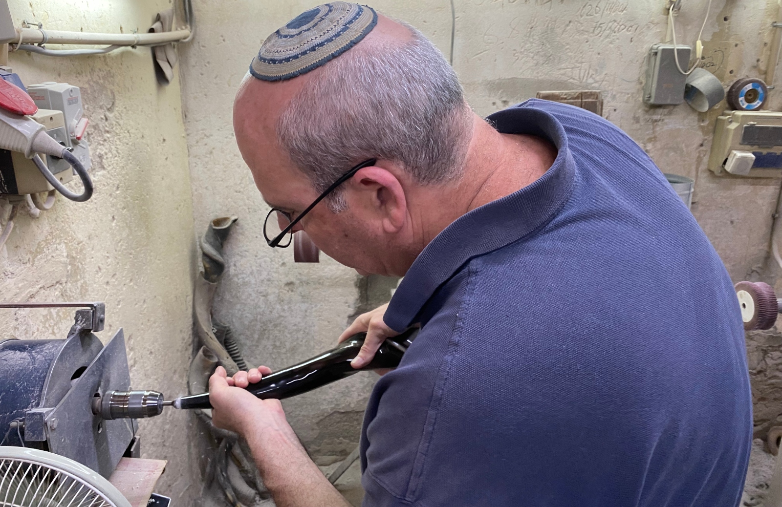 Eli Ribak drilling a mouthpiece into a shofar. Photo by Abigail Leichman A man wearing a kippah and glasses uses a power tool to shape a Shofar in a workshop.