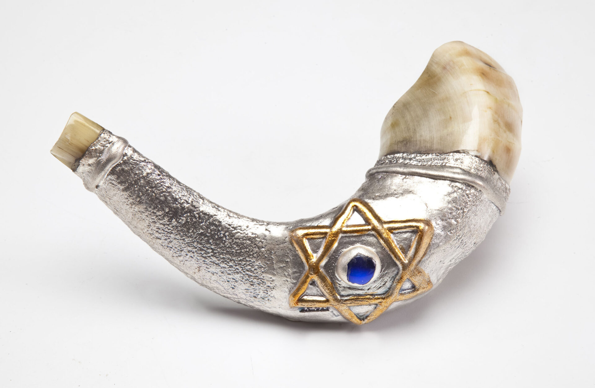 A silver-plated shofar at Barsheshet & Ribak. Photo by Eli Ribak A decorative shofar with a silver body and gold Star of David embellishment, featuring a blue gemstone in the center, against a plain white background.