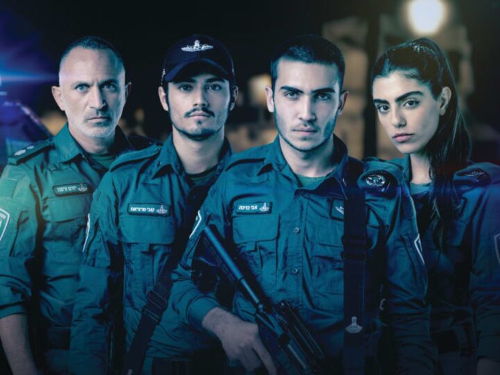 The cast of 'Borders,' in uniform stand together, three men and a woman. They appear serious and focused, with one holding a rifle. A police vehicle with flashing lights is visible in the background.