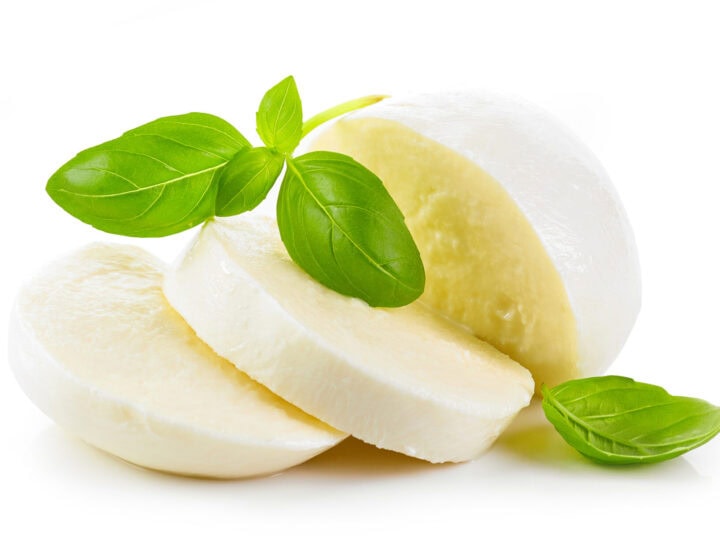 Three slices of fresh mozzarella cheese with green basil leaves, arranged on a white background.