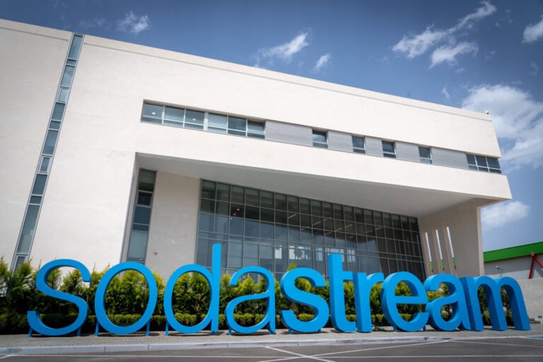 A large white building with windows on the facade. A large sign sits in front of it, which says the name of the company Sodastream in a sky blue color and all in lower case letters. 