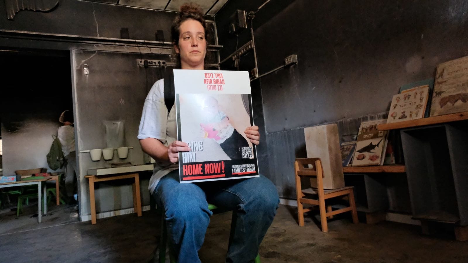 Yifat Zailer, a cousin of Shiri Bibas, in the destroyed daycare at Kibbutz Nir Oz holding a poster of Kfir Bibas. Photo by Adar Eyal