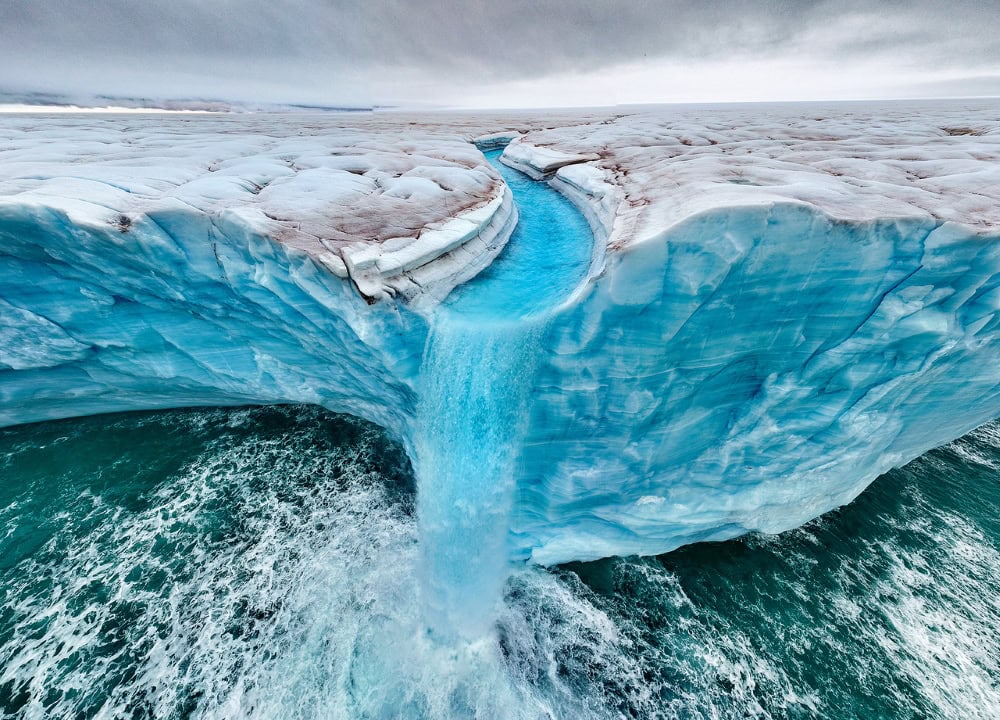 One of the TPOTY award-winning photos of waterfalls over Bråsvellbreen. As these waters flow into the ocean, they accelerate coastal threats worldwide. Photo by Roie Galitz/TPOTY